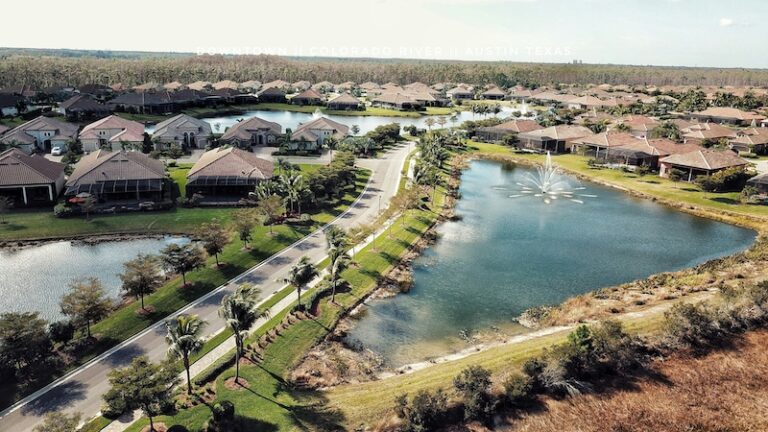 Aerial view of a suburban neighborhood in Austin, Texas, with rows of houses, ponds, landscaped yards, and a fountain in the center lake—ideal for homeowners considering lightning protection or planning to install a lightning rod.