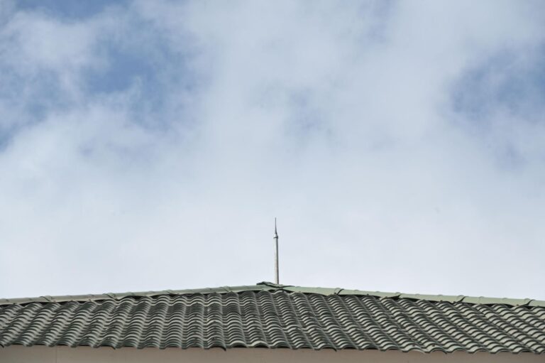 A green tiled roof with lightning protection, featuring a lightning rod on top and set against a cloudy sky.